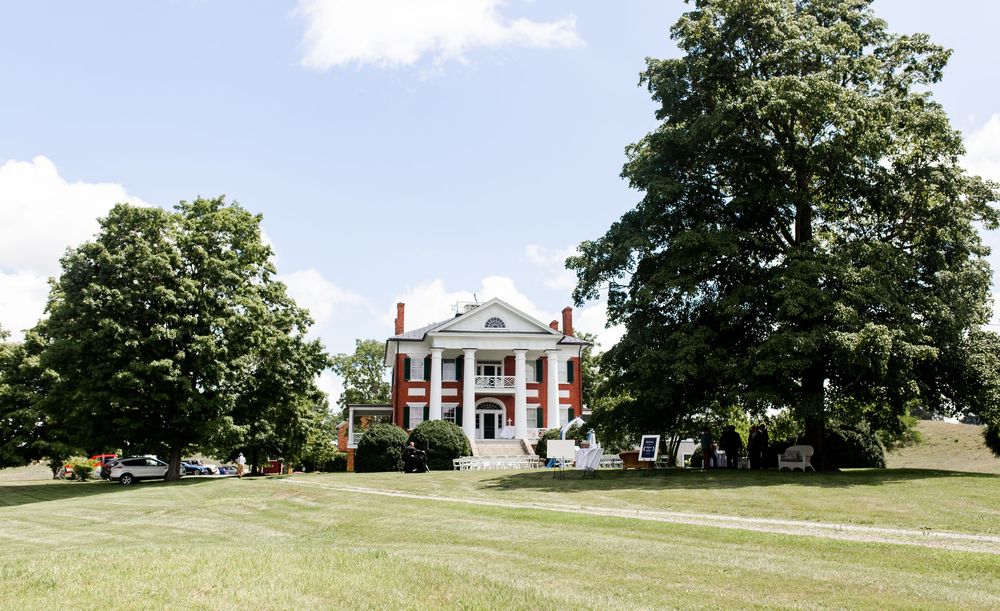 Grand white-columned mansion surrounded by large trees on a lush green lawn.