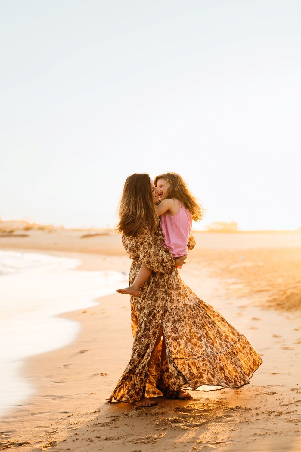 Mother and child in flowing dress embraces on sandy beach at golden sunset creating movement in Sydney