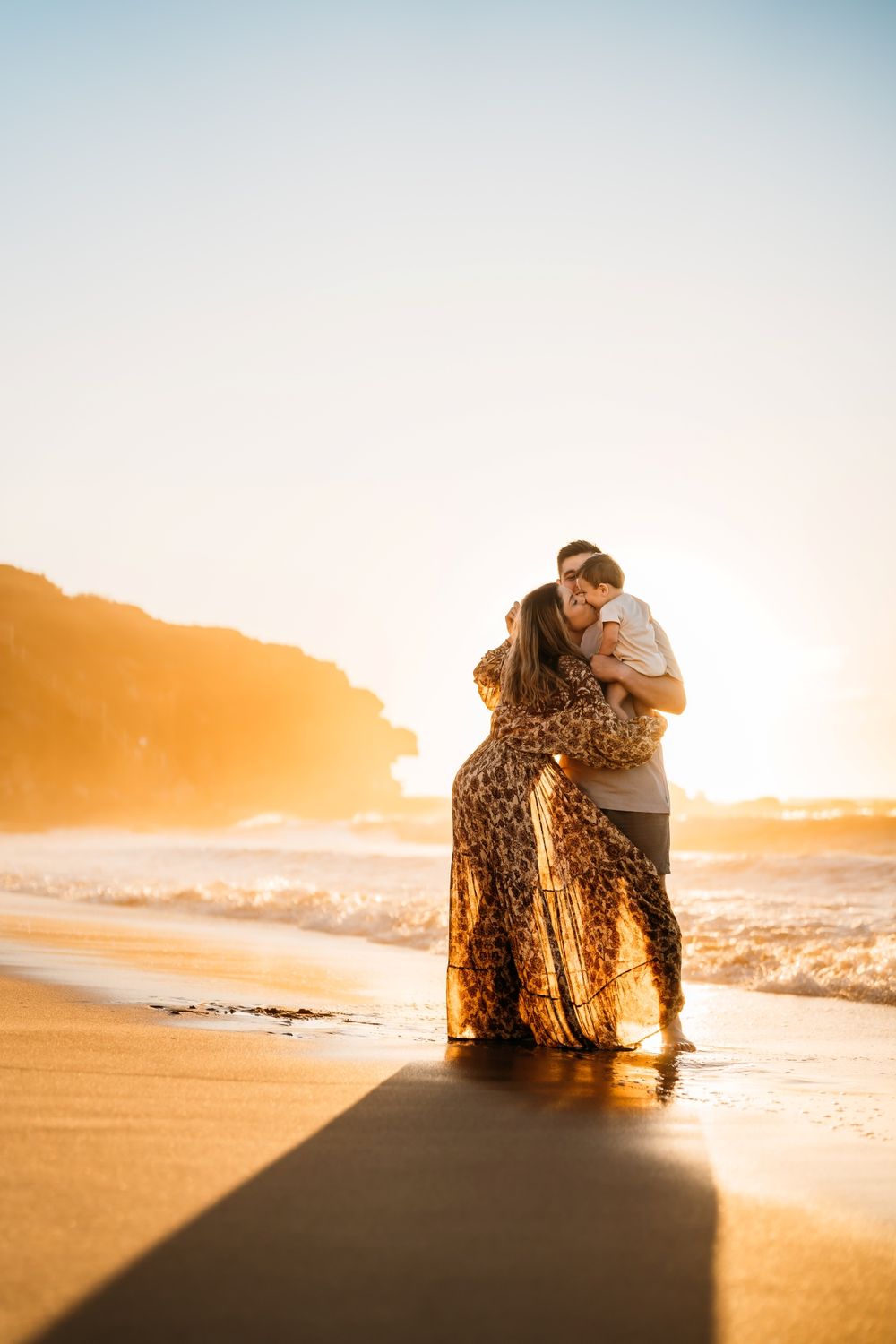 A family embraces on a sandy beach at sunrise casting long shadows across the golden shore.