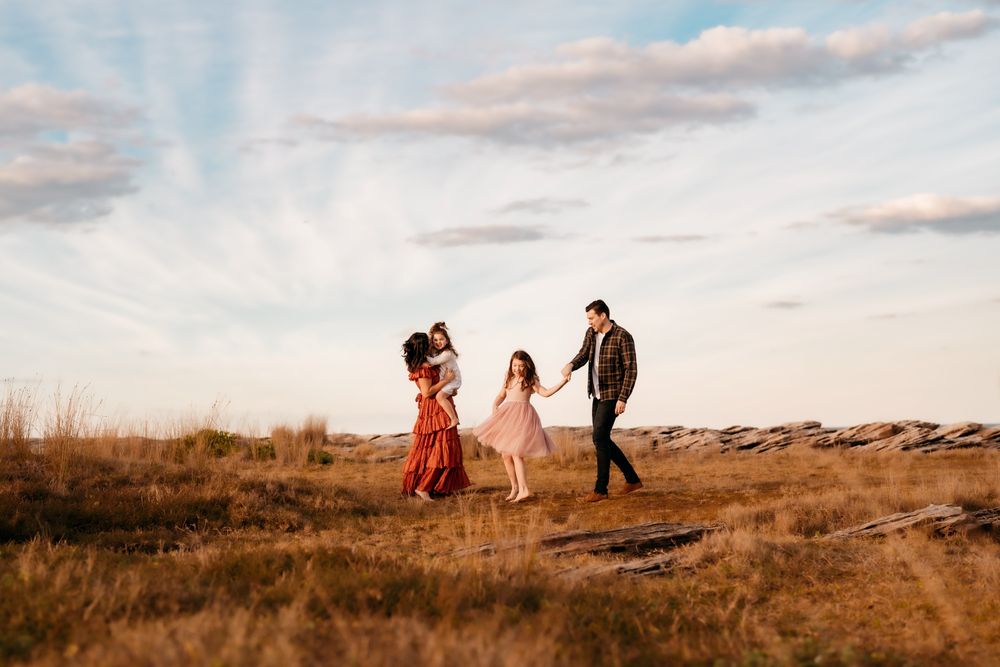 A family play and have fun in a golden field at sunset with soft clouds in the sky above.