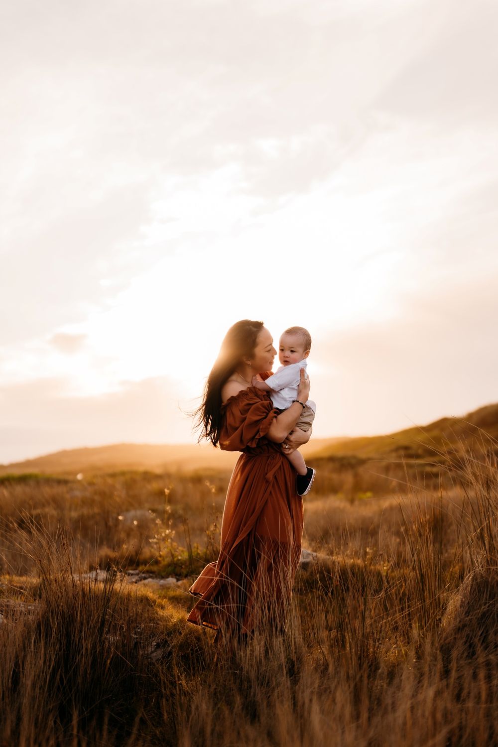 A parent and child share a tender moment in a golden field at sunset, creating a heartwarming silhouette.