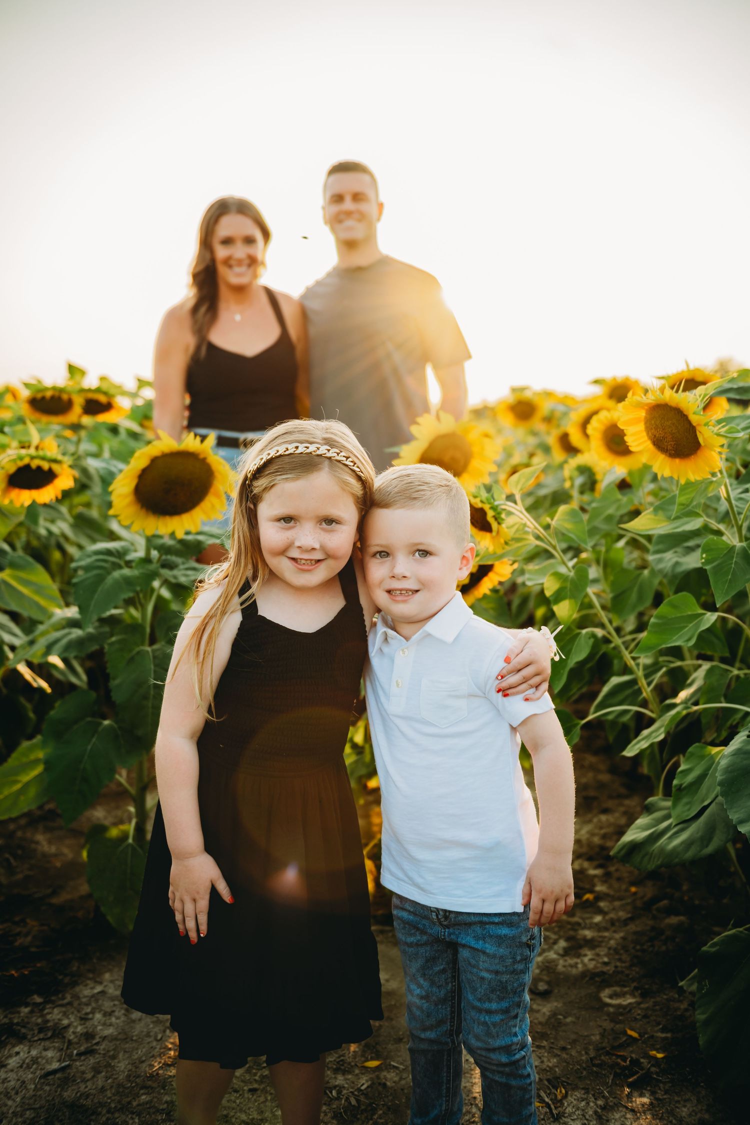 Family photo session in a vibrant sunflower field at sunset with golden light streaming through.
