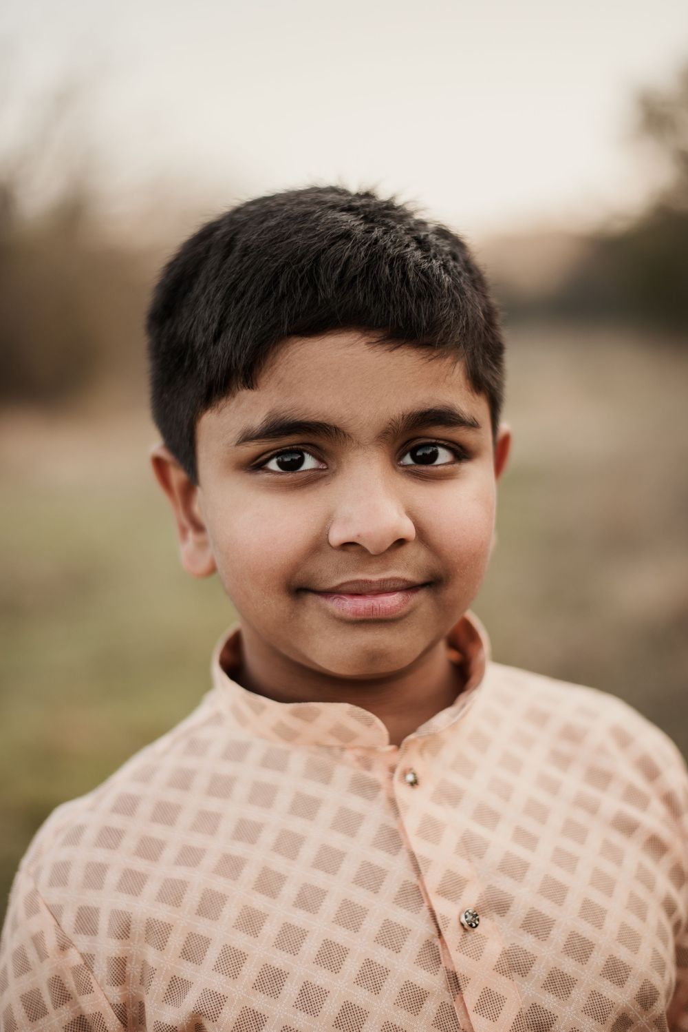 Young boy in a checkered kurta smiles outdoors during a family portrait session.