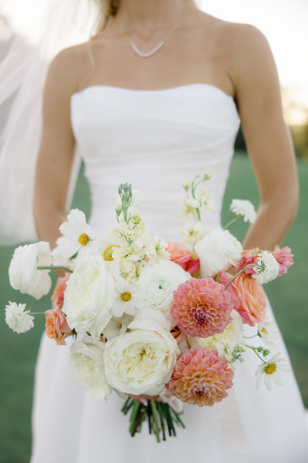 Close-up of a bridal bouquet featuring white peonies, coral dahlias, and soft pink roses.