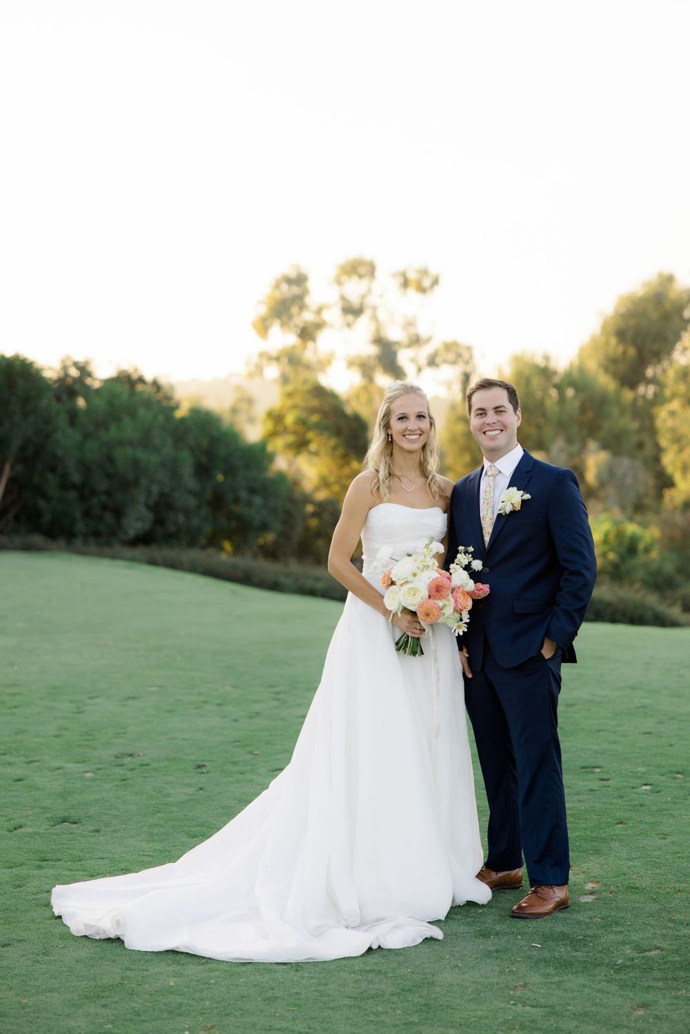Newlyweds posing for portraits on a manicured lawn during sunset.
