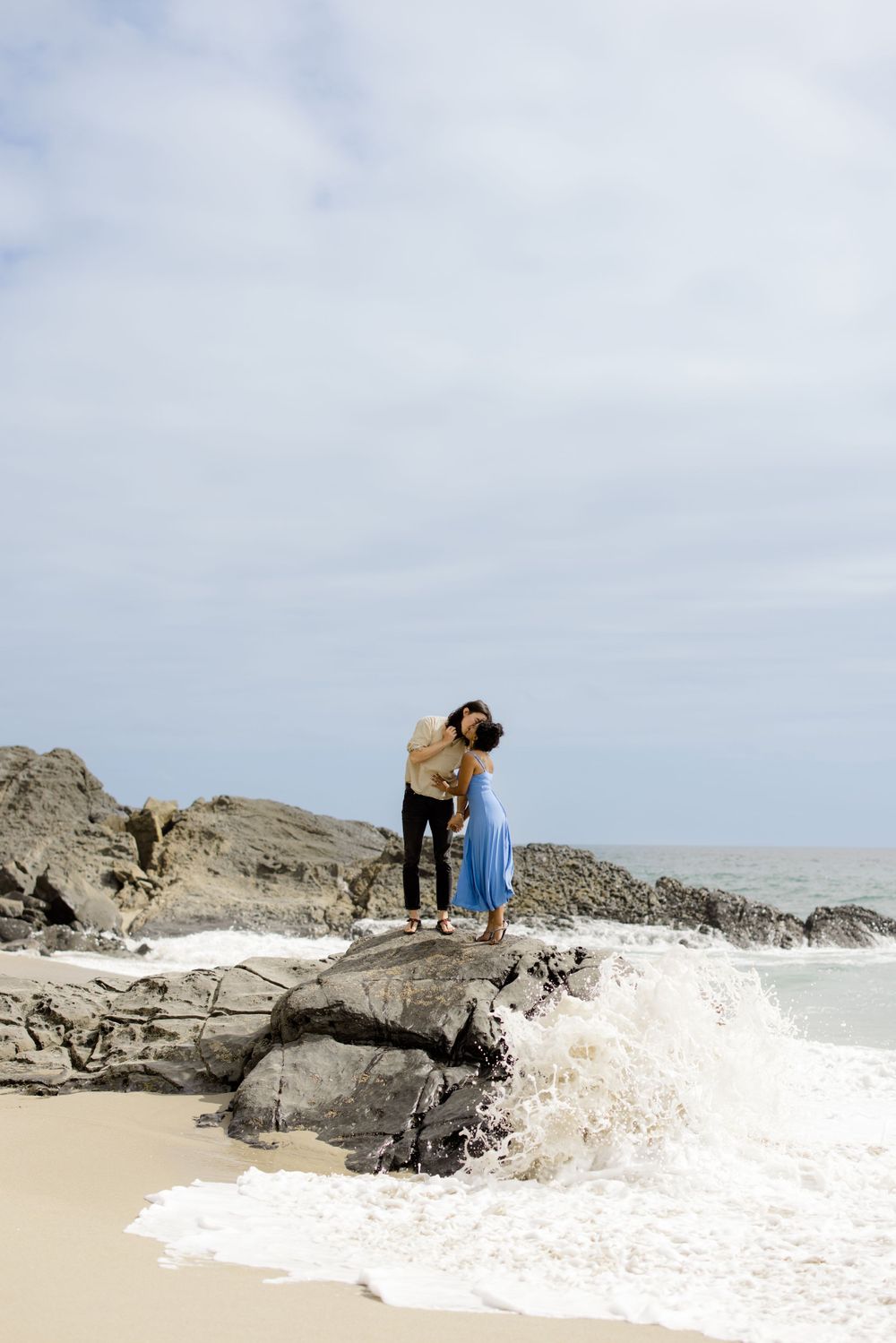 A couple shares a tender moment on coastal rocks as waves crash below.