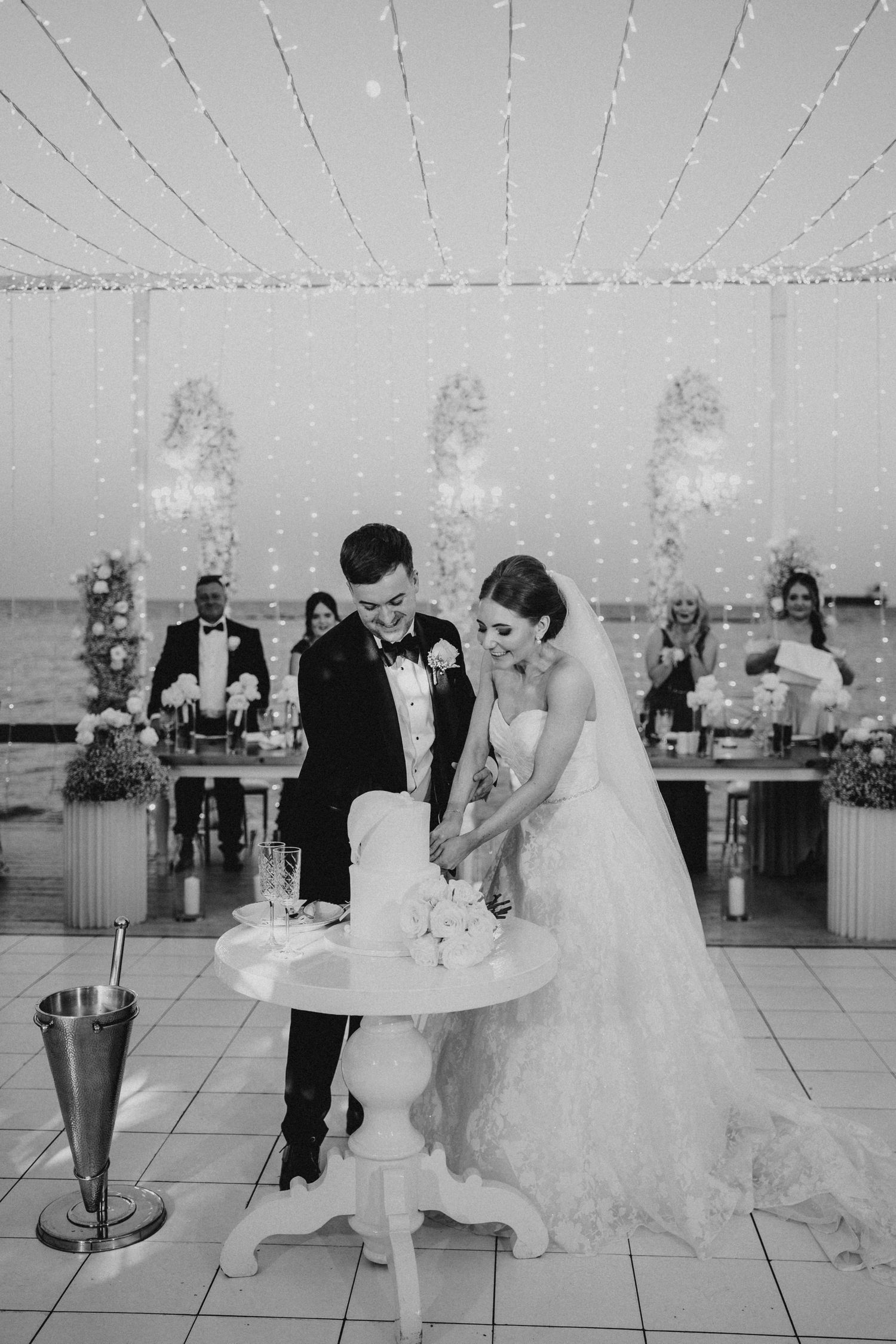 A couple cuts their tiered wedding cake against a backdrop of geometric shapes and purple lighting.