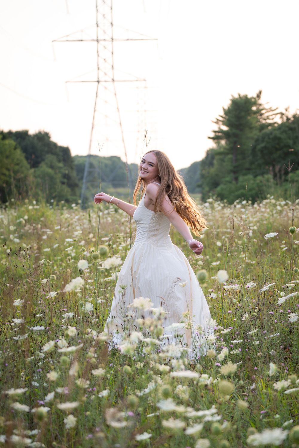 Young woman in white gown twirling joyfully in a wildflower meadow at golden hour.