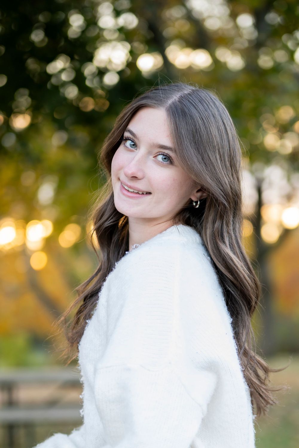 Autumn outdoor portrait with warm bokeh lighting and white fuzzy coat.