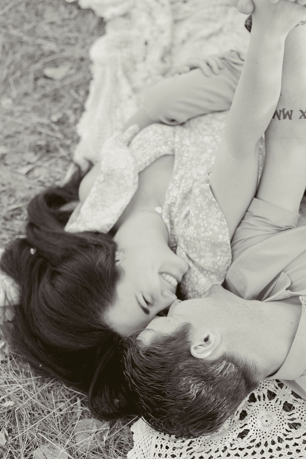 Romantic black and white portrait of couple lying on lace blanket outdoors.