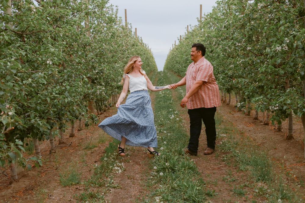 Couple walking through rows of apple trees in orchard during photo session.