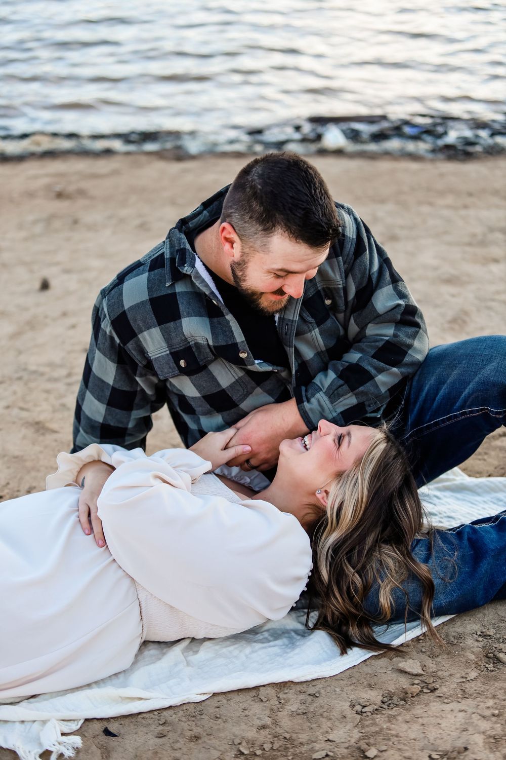 Romantic beach photoshoot with couple lying on sand near water.