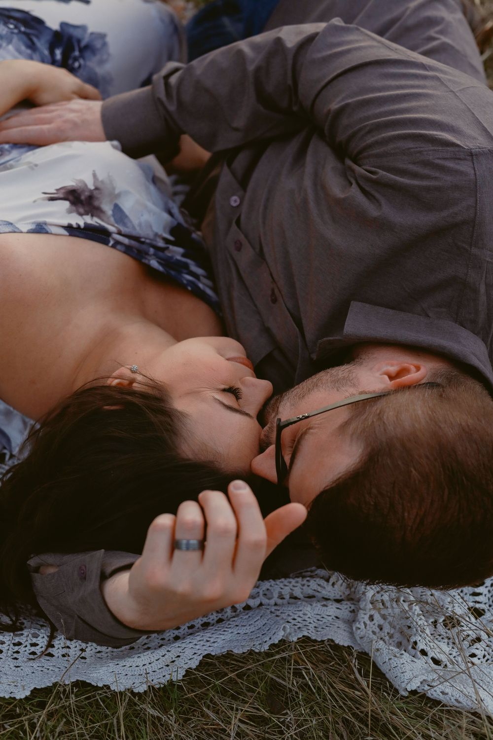 Intimate couple portrait session on white lace blanket in natural setting.