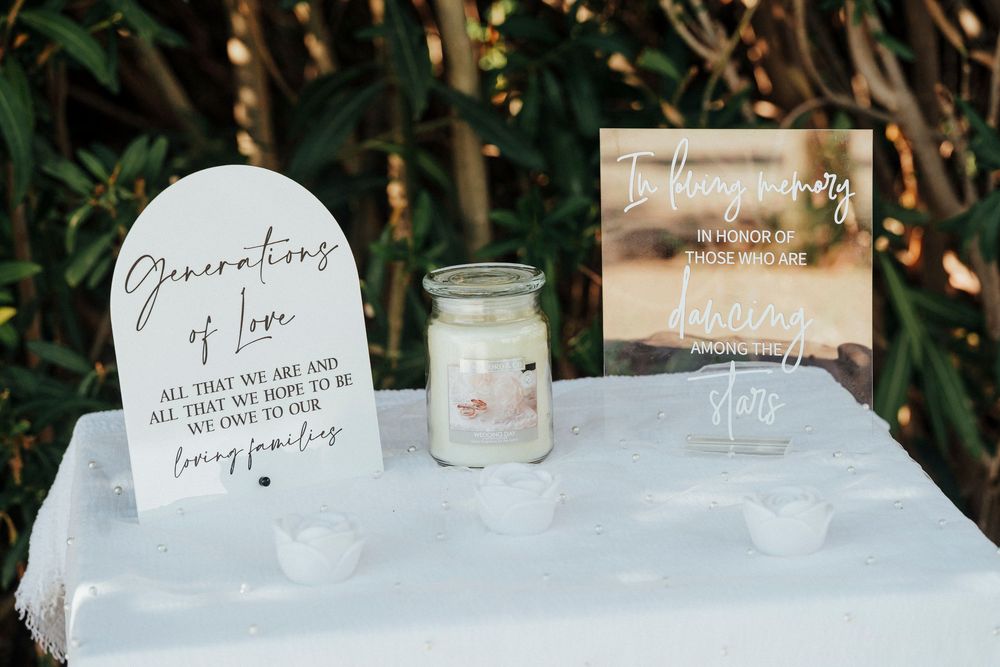 Wedding memorial signs and candle displayed on white table with greenery backdrop for remembrance of loved ones.