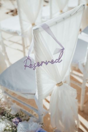 White fabric chair covers with purple 'Reserved' text written on them at an elegant wedding ceremony setup.