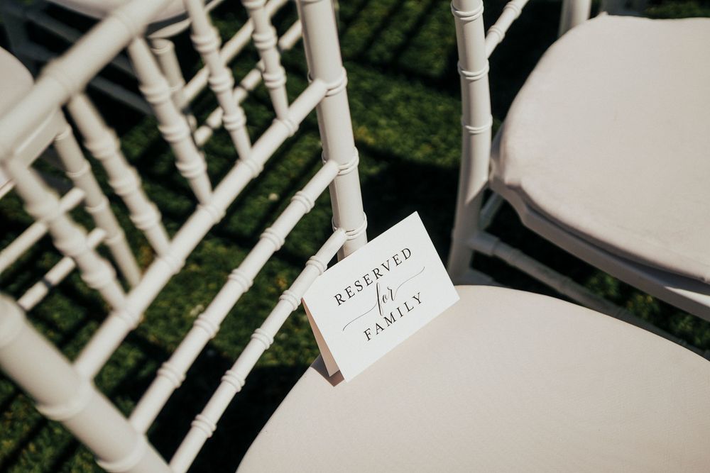 White wooden chairs arranged in rows outdoors for an elegant garden wedding ceremony.