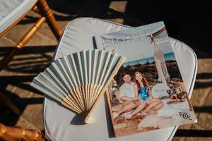 A vintage paper fan and polaroid photograph displayed on a white surface in warm sunlight.