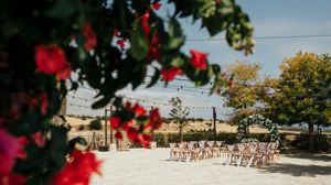 Panoramic view of a beachfront wedding ceremony setup with white chairs and red flowers in the foreground.