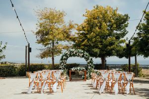 Outdoor wedding ceremony setup with white chairs and orange floral arrangements along the aisle on a sunny day.