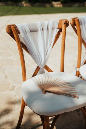 White folding chairs with sheer fabric draping elegantly arranged for an outdoor wedding ceremony.