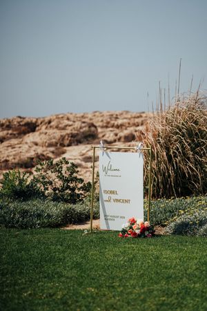 White memorial plaques with red flowers sit along a grassy hillside against a soft-focus background.