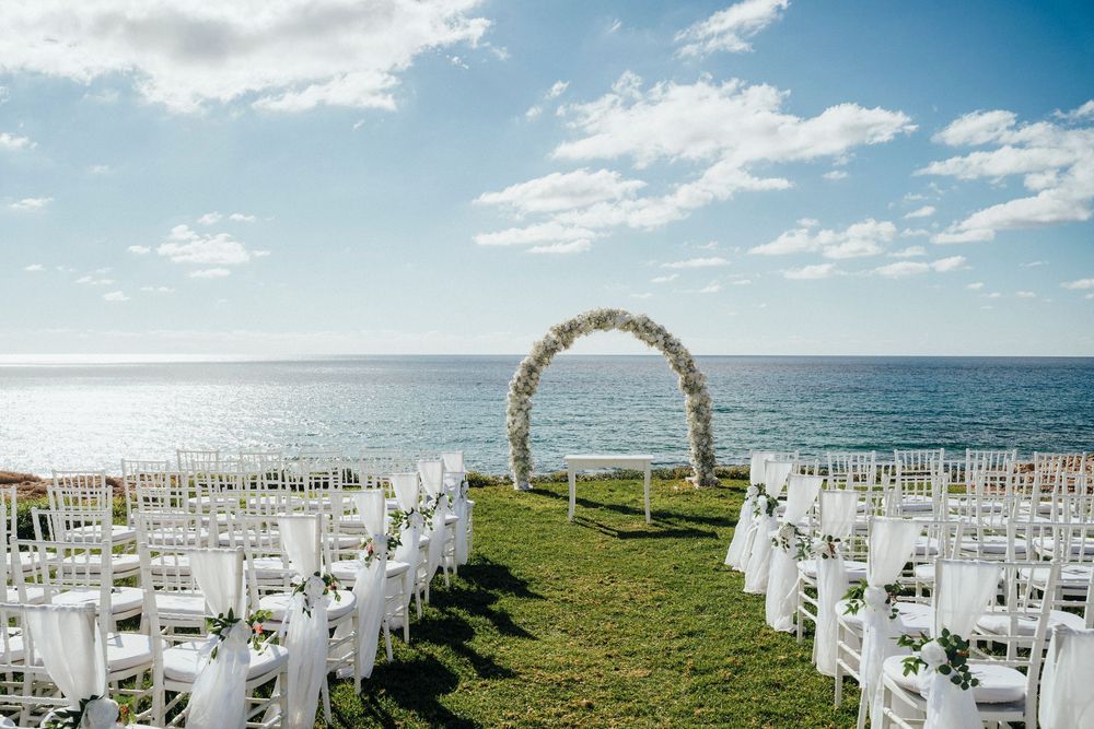White chairs arranged in rows for an outdoor beach wedding ceremony with ocean views and blue skies overhead.