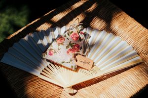 Decorative hand fans with floral patterns and delicate details lay arranged on a wooden surface in warm lighting.
