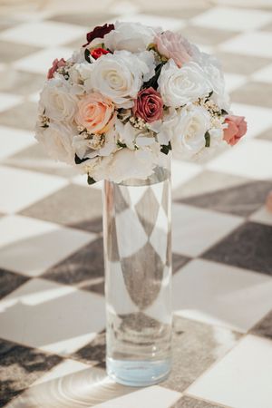 A romantic bouquet of white and pink roses arranged in a tall clear glass vase on a checkered floor.