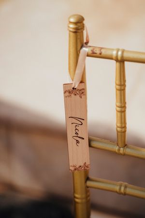 Close-up view of a wooden name tag with cursive text attached to a gold-colored Chiavari chair.