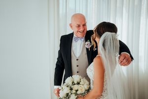 A bride and groom share a joyful moment during their wedding ceremony in front of white curtains.