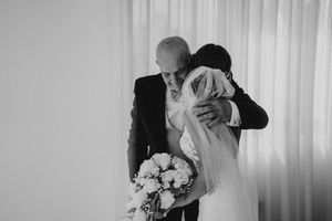 A romantic wedding couple shares a tender kiss during their ceremony while holding a white floral bouquet.