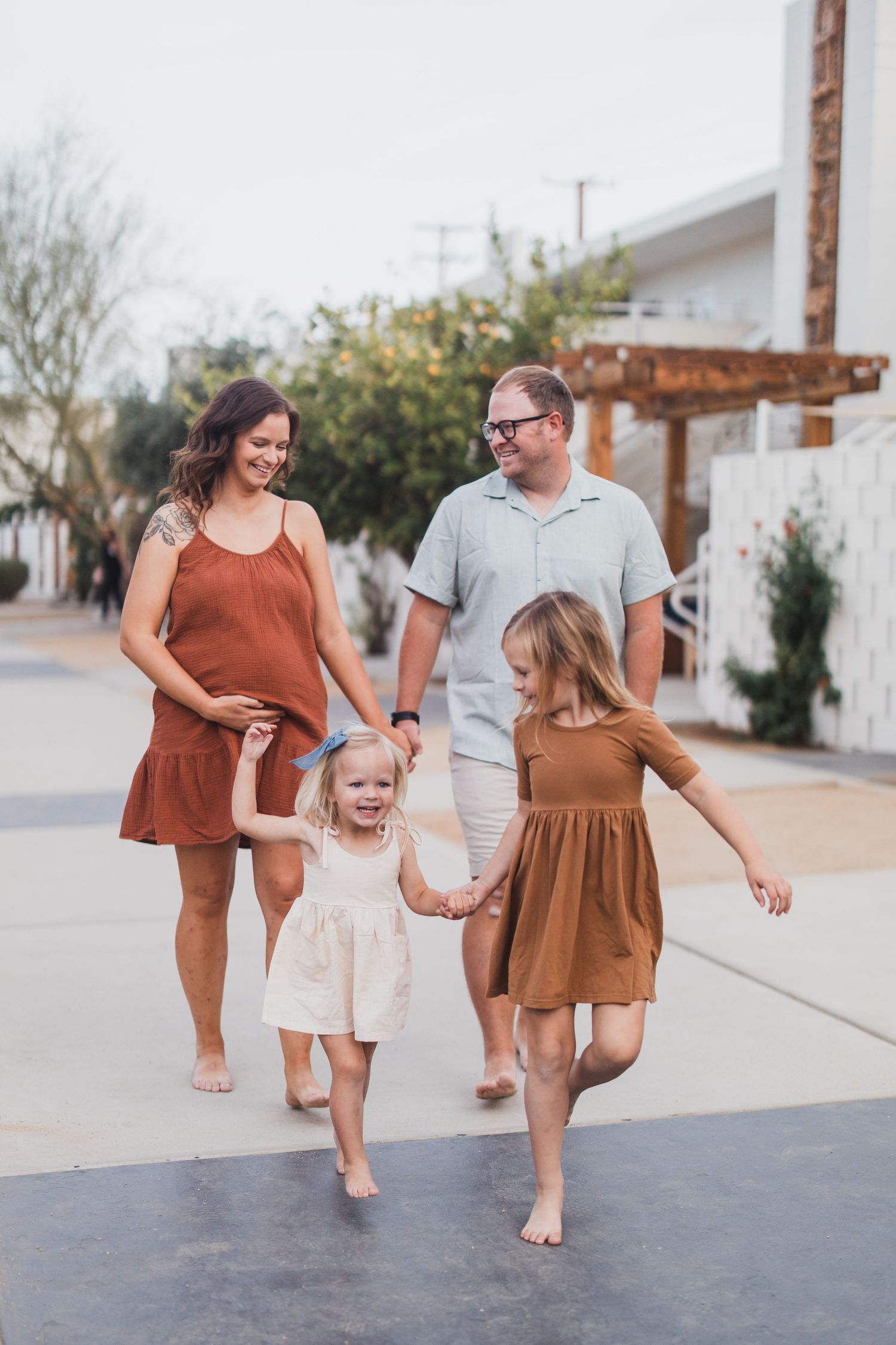 A joyful barefoot family walks together on a sidewalk in coordinating rust and cream colored outfits.