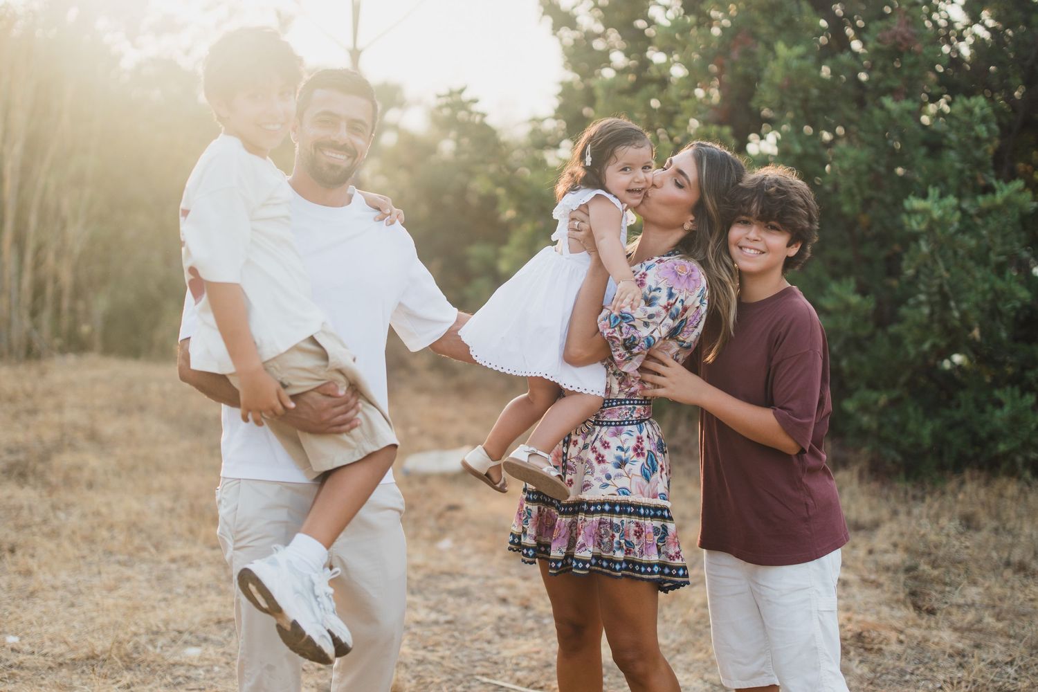 Family photoshoot session in a park with natural sunlight and greenery in the background.