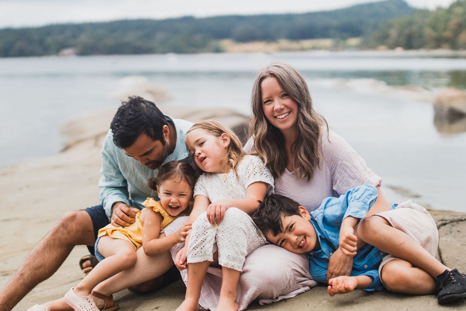 Family playing and laughing together while lying on sandy beach at sunset.
