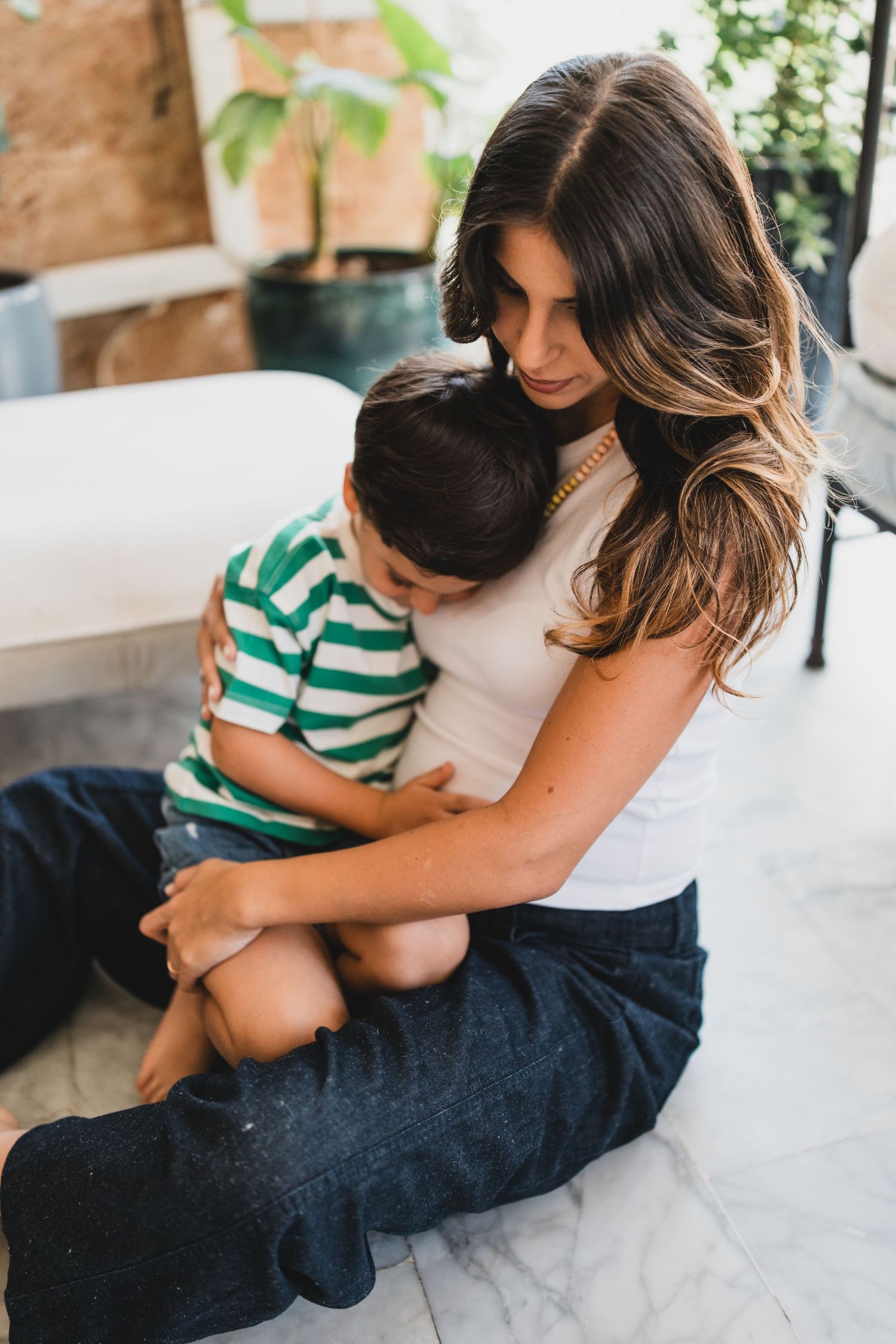 A parent and child share a tender embrace while sitting together on a textured floor.