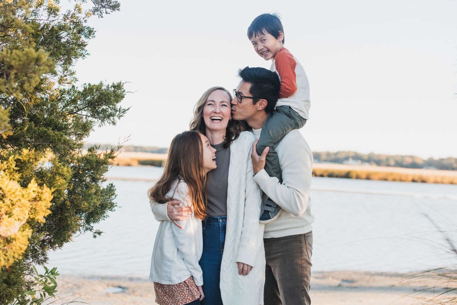 A family enjoys a playful moment together outdoors near a lake on a sunny autumn day.