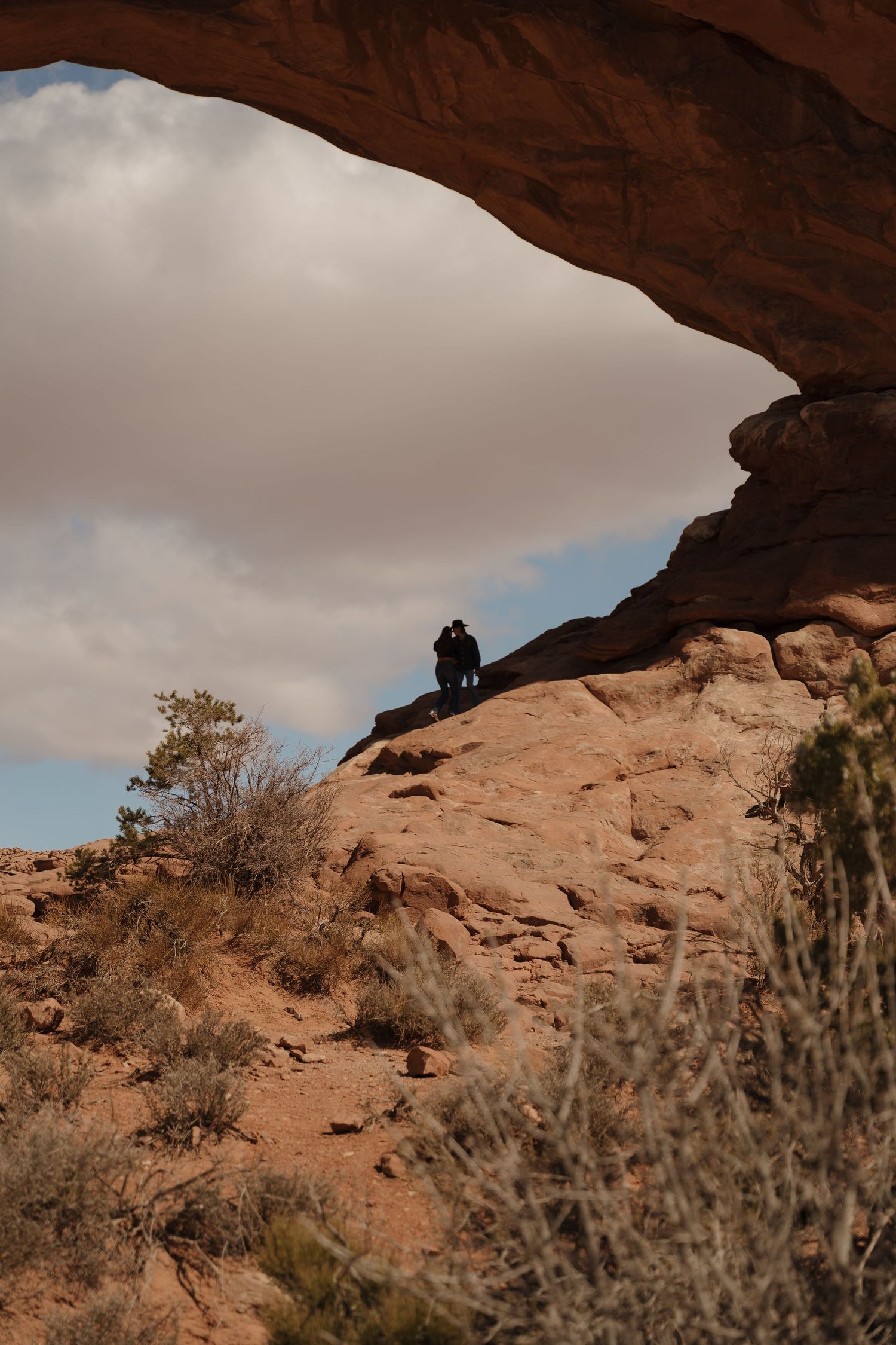 Natural rock arch formation in desert landscape with silhouetted figures.