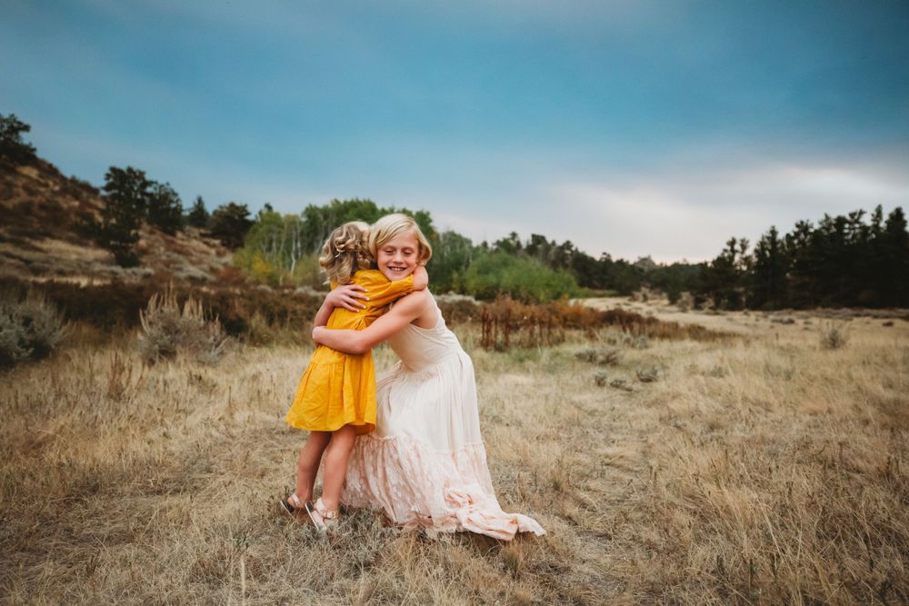Two little girls hug in green and brown field at sunset in Dickson, TN