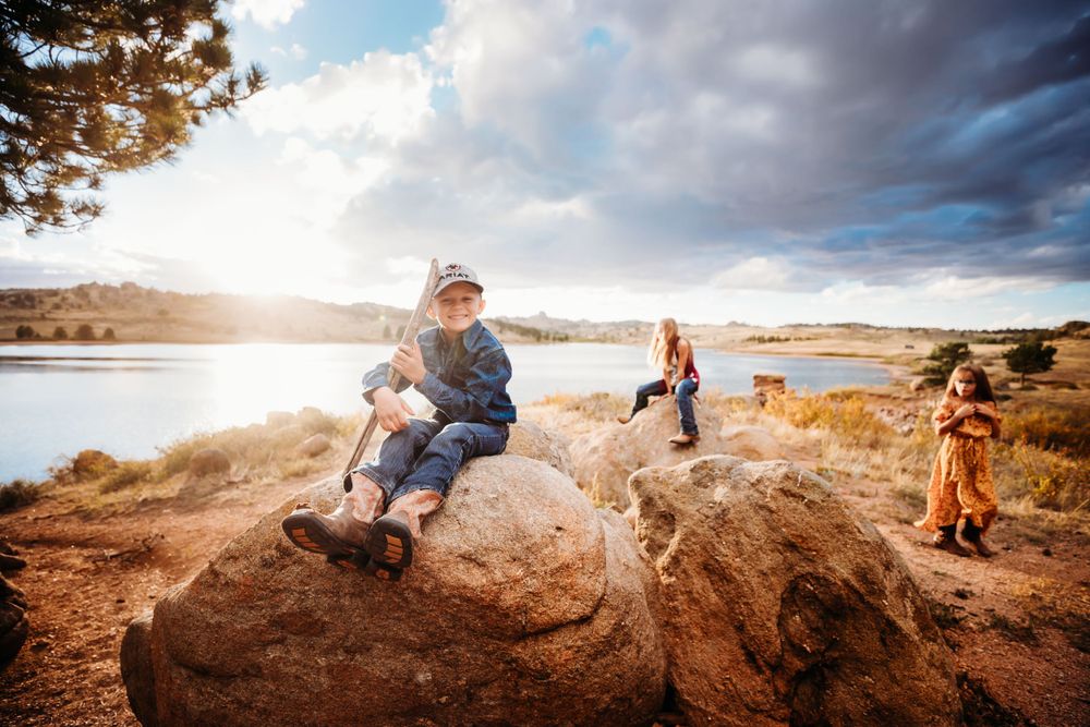 Little boy holds a branch sitting on a rock smiling with other kids in the background in Dickson, TN