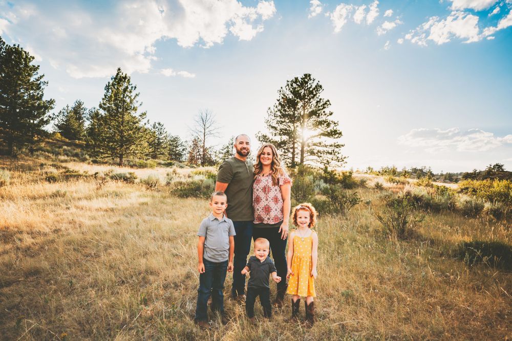 Mom, Dad, and three kids smiling in a green and brown field with blue sky in Dickson, TN