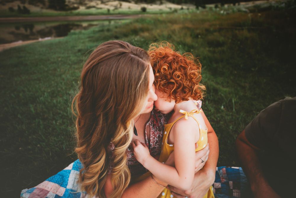 Mom holding red haired little girl with field and water in the background in Dickson, TN
