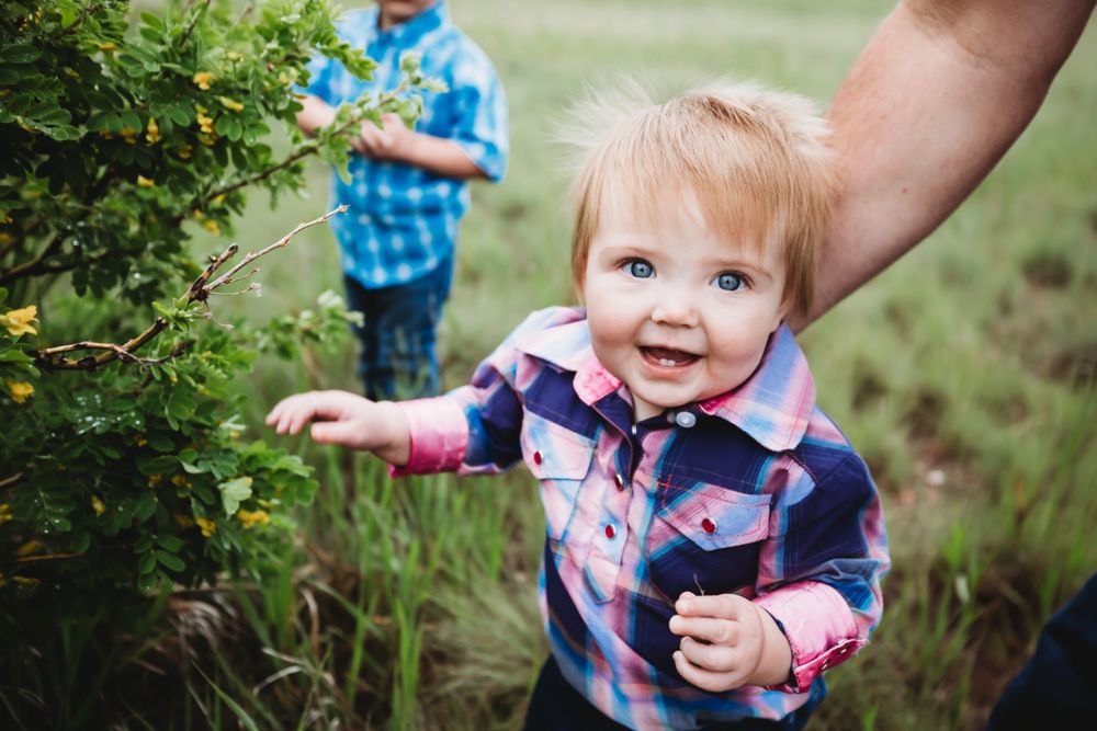 Little girl in plaid button down shirt smiles while her dad helps her stand in Dickson, TN