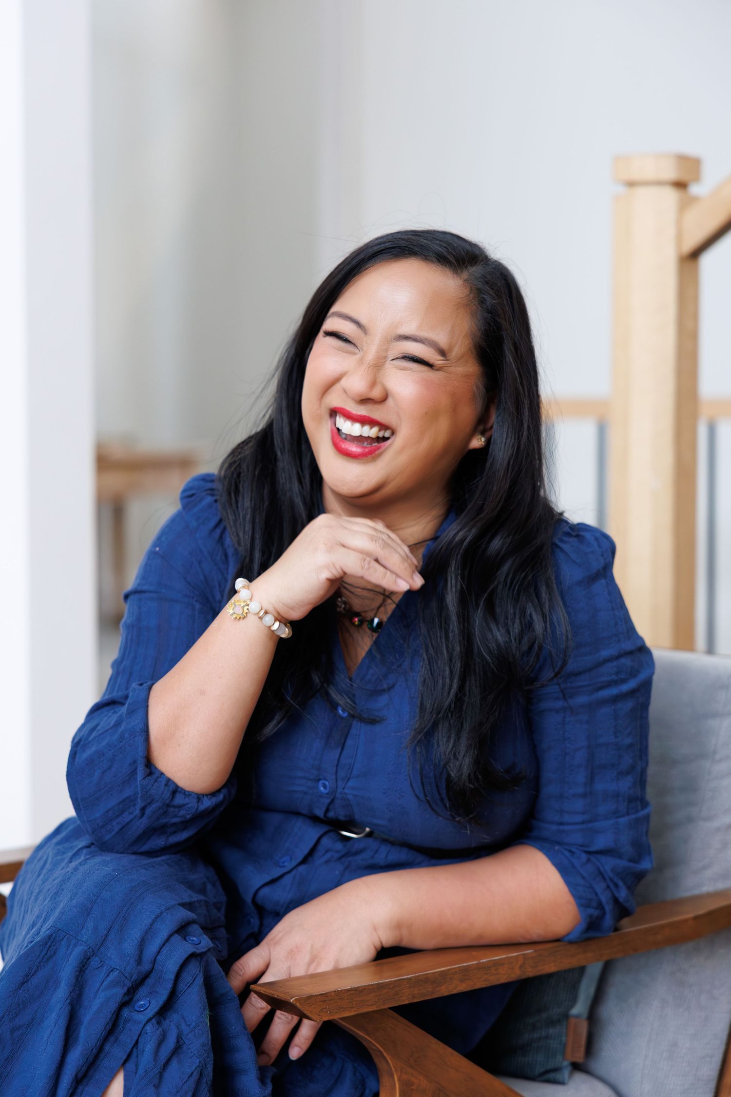Professional wearing navy blue shirt sits casually on grey couch in bright indoor setting.