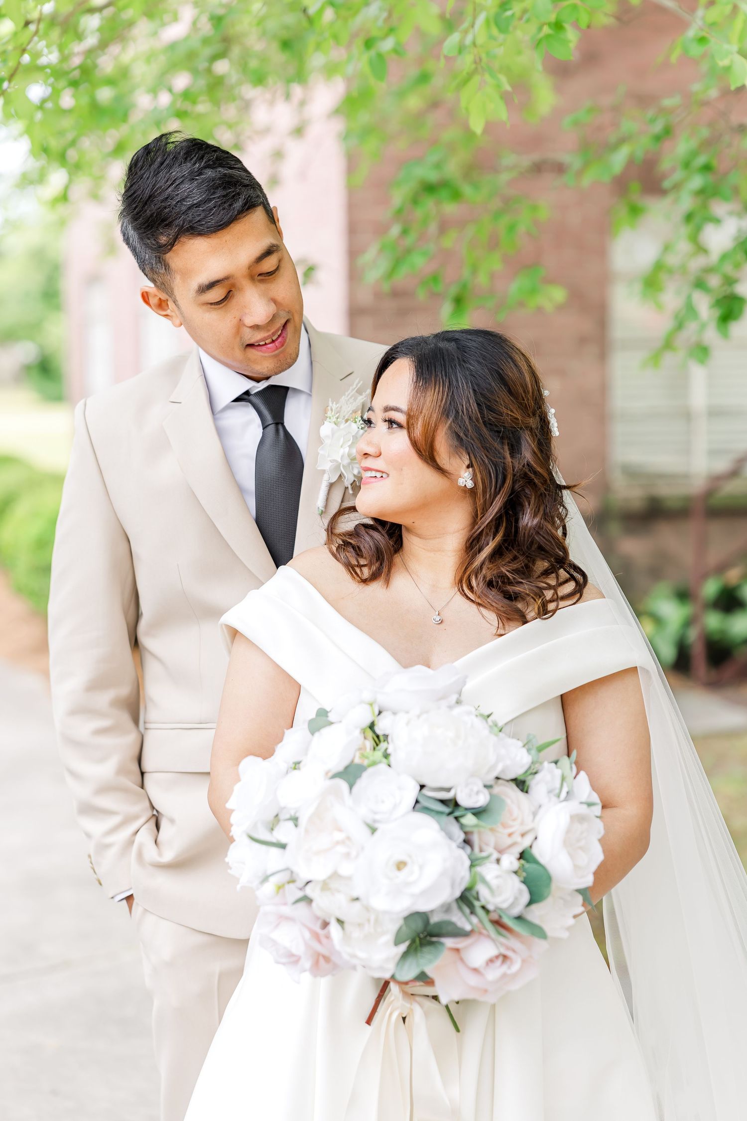 Romantic wedding couple embraces while holding white floral bouquet in outdoor garden setting.