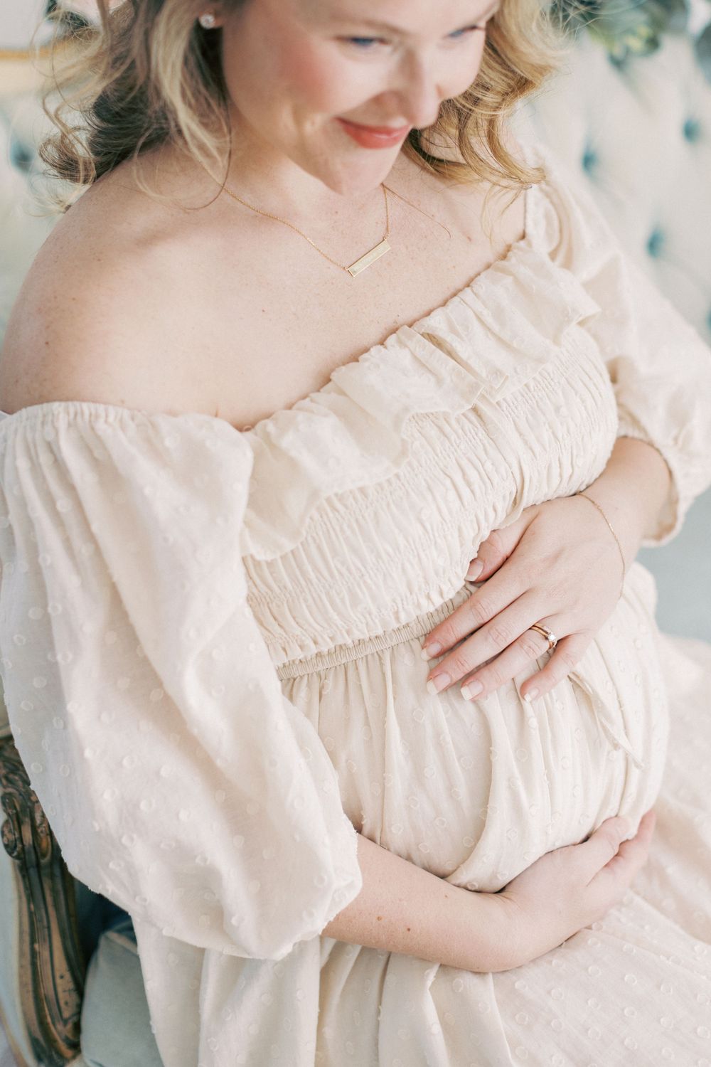 A delicate maternity photo featuring an off-shoulder cream dress with billowy sleeves and a gentle smile.