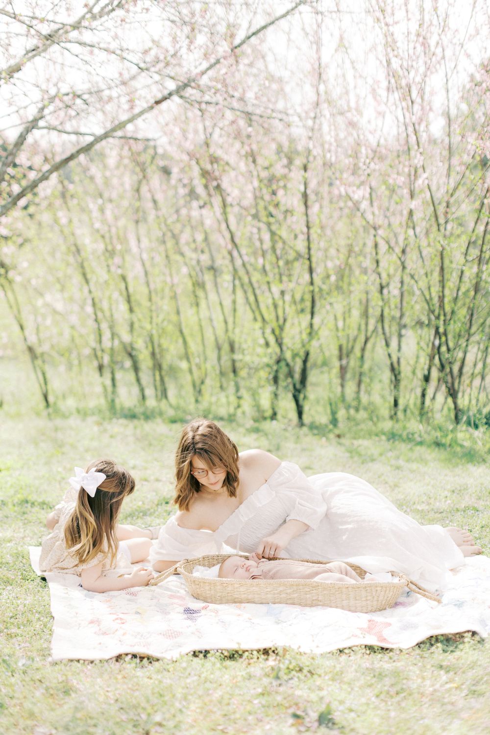 Two people in white dresses sitting on a picnic blanket in a dreamy spring garden with blossoming trees.