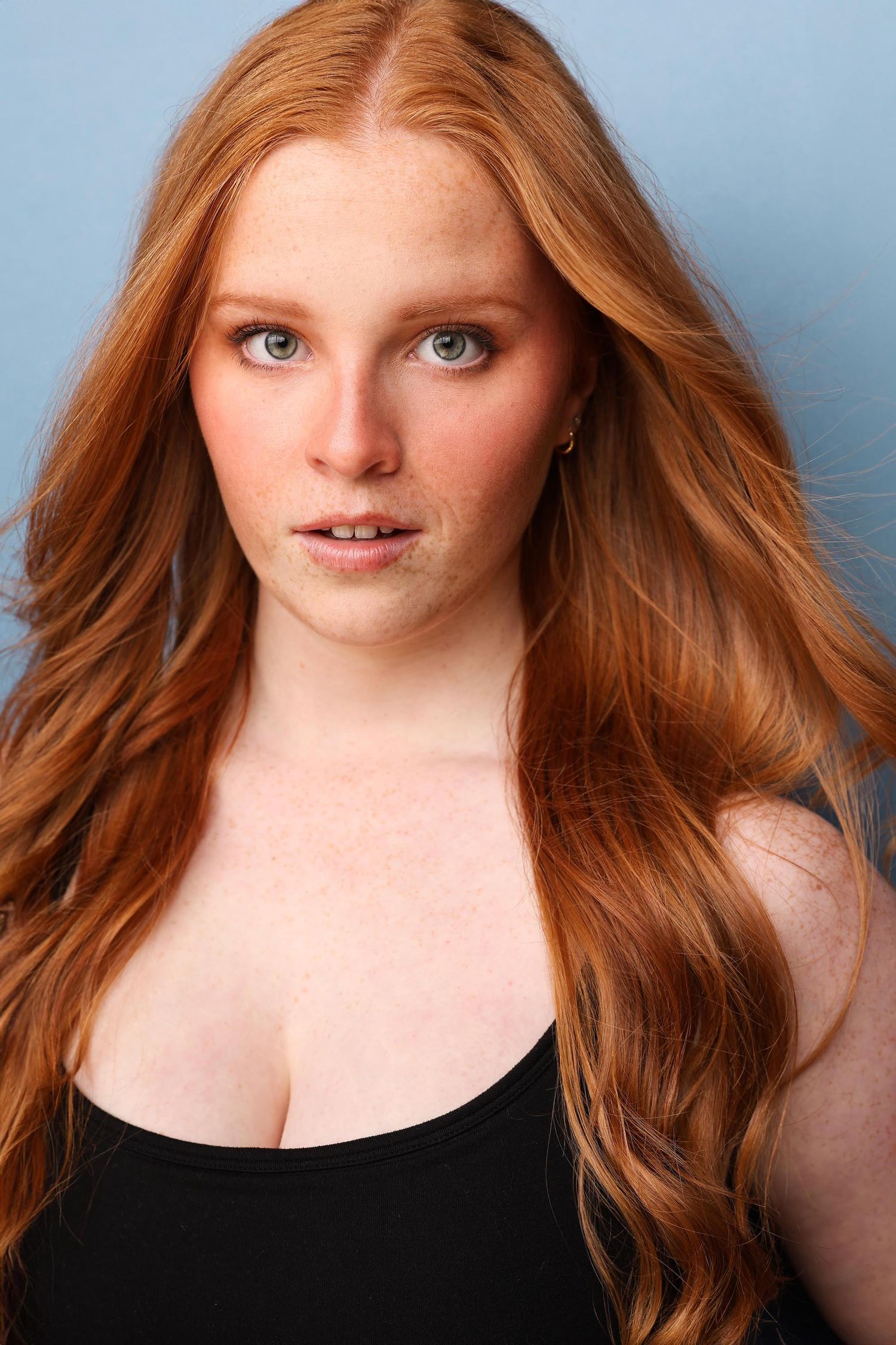 Professional headshot portrait of person with curly dark hair wearing an unbuttoned navy blue shirt against neutral background.
