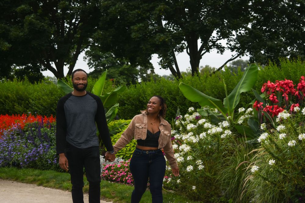 A couple walks together through a colorful garden with red flowers and greenery.