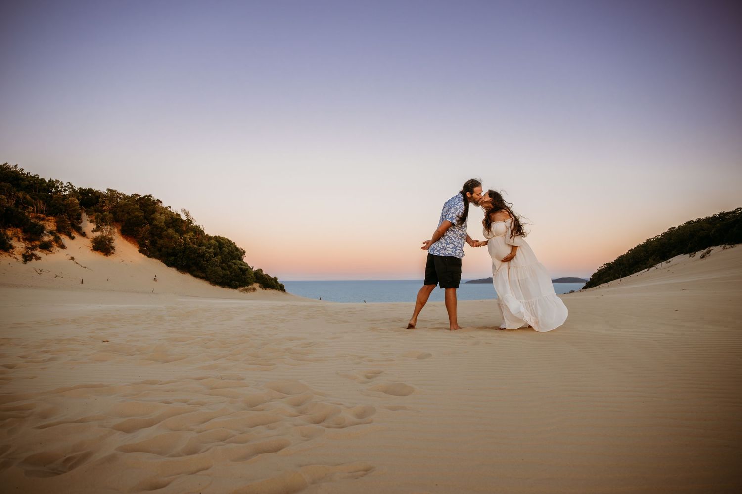 Couple sharing an intimate moment at sunset on rocky coastal overlook.