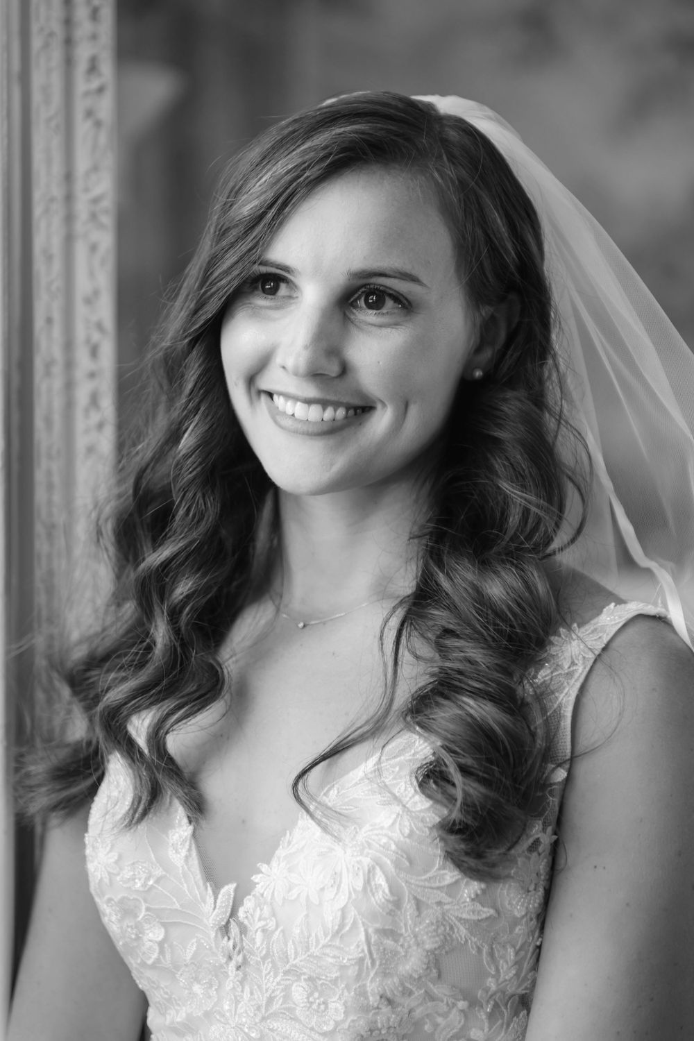 Black and white portrait of a bride wearing a lace wedding dress and veil with flowing wavy hair and bright smile.